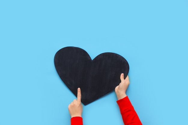 Woman holds a chalk board in the shape of a heart on a blue background for Valentine's Day