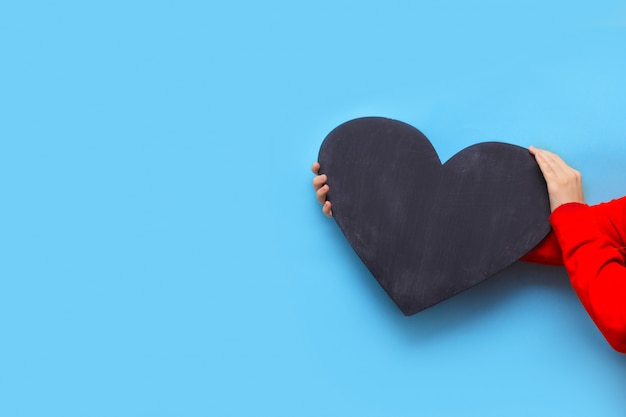 Woman holds a chalk board in the shape of a heart on a blue background for Valentine's Day