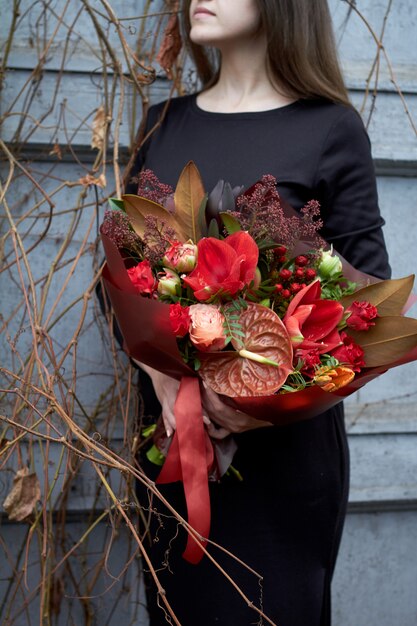 Woman holds chic autumn bouquet in red colors in vintage style outdoors