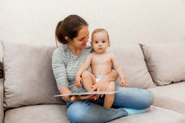 A woman holds a child in her arms and reads a book to him. mother and child on the couch.