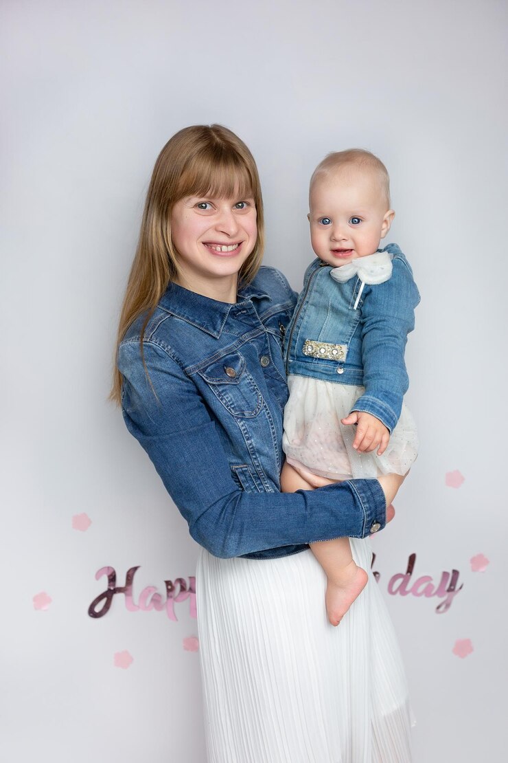 a woman holds a child and smiles with the words happy birthday on the wall behind her