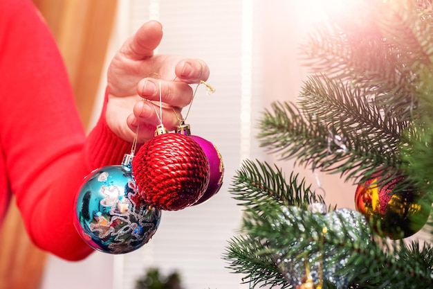 A woman holds Christmas decorations in her hand near a Christmas tree