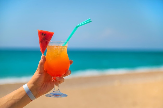 A woman holds a cocktail in her hand against the background of the sea. Selective focus. Nature.