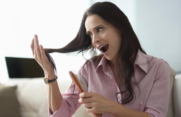 Woman holds comb in her hand and looks at her hair in panic