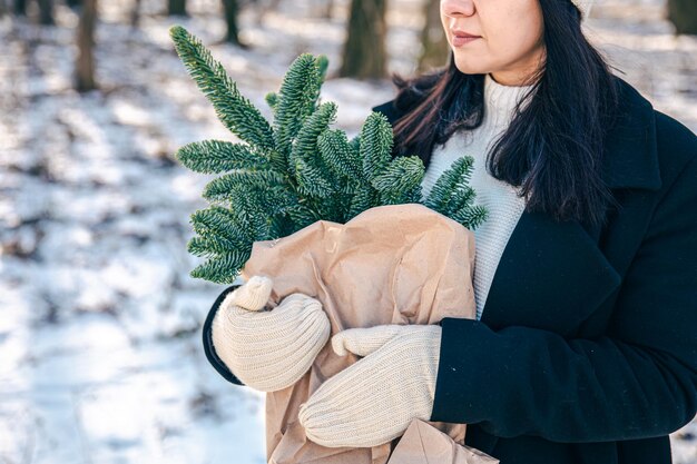 Una donna tiene una borsa artigianale con rami di albero di natale nella foresta invernale