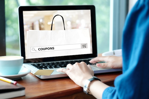 Woman holds credit card while uses laptop computer with shopping on line mock up.