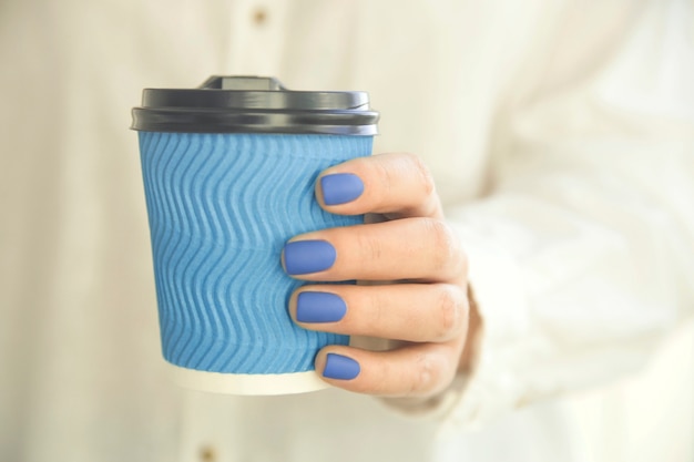 Photo woman holds a cup of coffee in her hands with blue manicure.