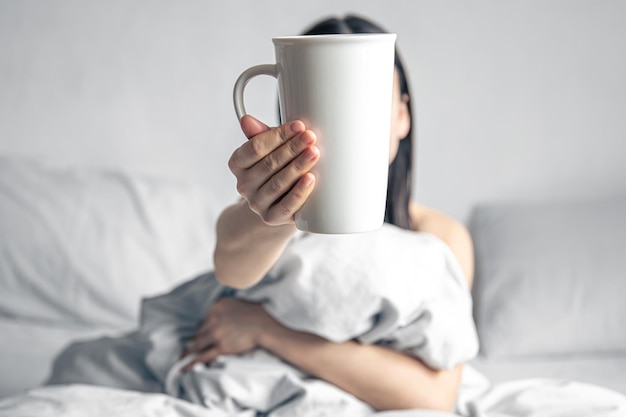 A woman holds a cup of coffee while lying in bed