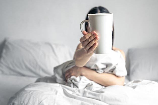 A woman holds a cup of coffee while lying in bed