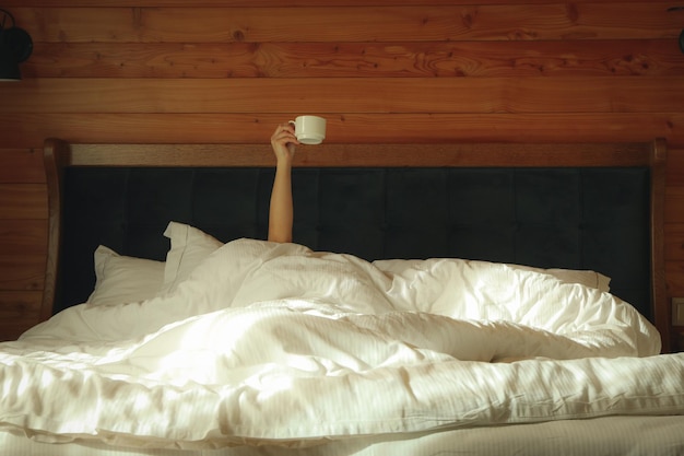 Woman holds cup and lying in bed