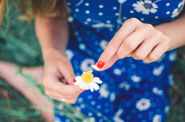 Woman holds a daisy flower and tears off the petals