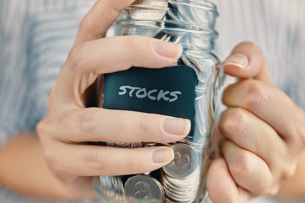 Woman holds dividends from stocks in glass jar bottle with coins and sticker in hands concept of ear...