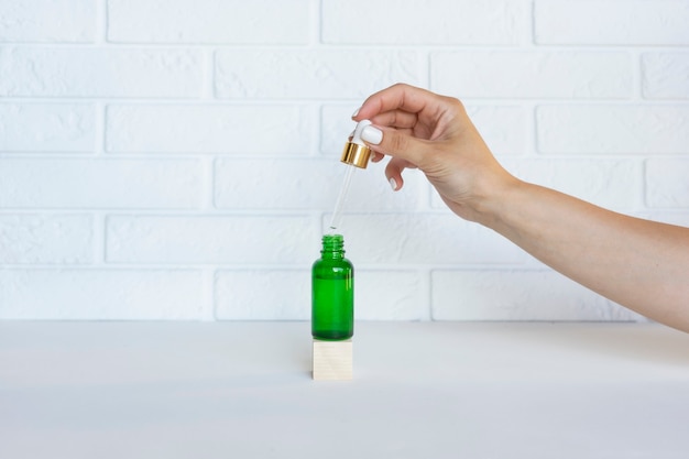 A woman holds a dropper of the bottle with serum or natural essential oil