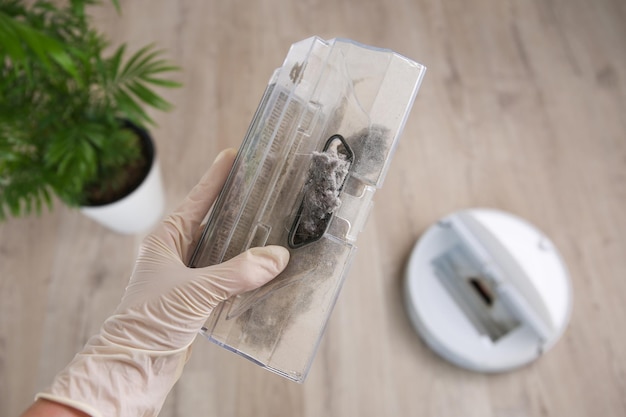 A woman holds a dust collector with garbage The concept of a robot vacuum cleaner cleans the floors in the house