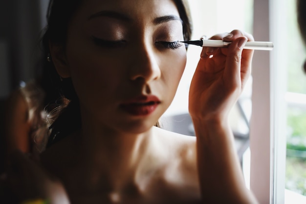 Woman holds eyeliner before bride's eye