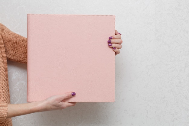 A woman holds a family photobook. the person looks at the photo book. sample pink photo album.  wedding photoalbum with  leather cover.