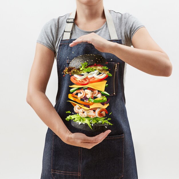 Woman holds a flying homemade burger from fresh organic ingredients on a light background