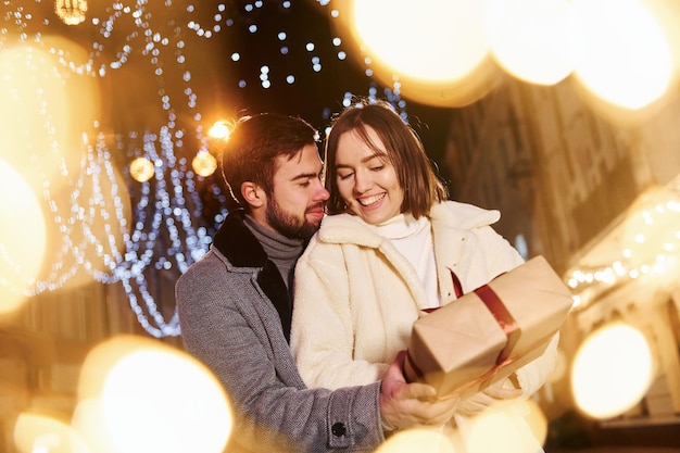 Woman holds gift box Happy young couple celebrating New year outdoors on the street