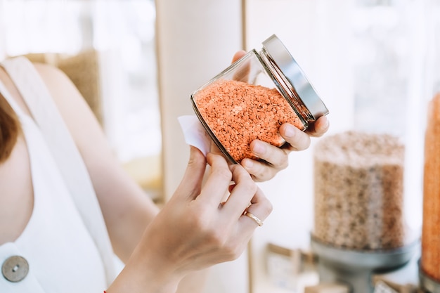 woman holds glass jar with red lentils in plastic free grocery store girl buying in zero waste shop