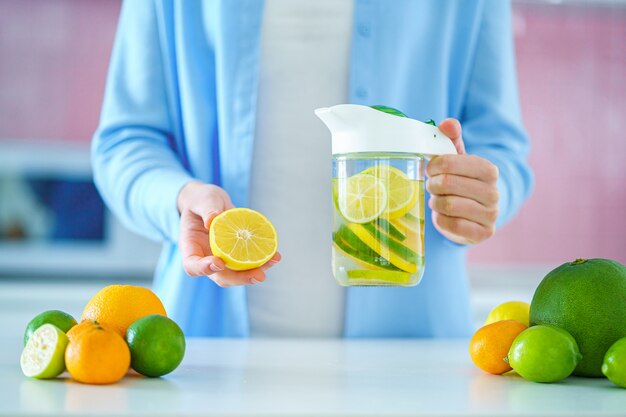 Woman holds glass jug with refreshing infused detoxification citrus water for vitamin detox drink.