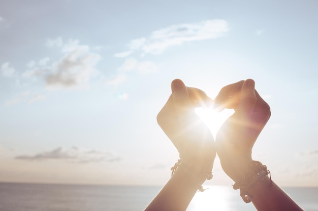 Woman holds hands up to sky in the shape of a heart