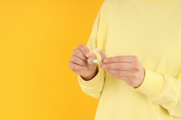 Woman holds hearing aid on yellow background