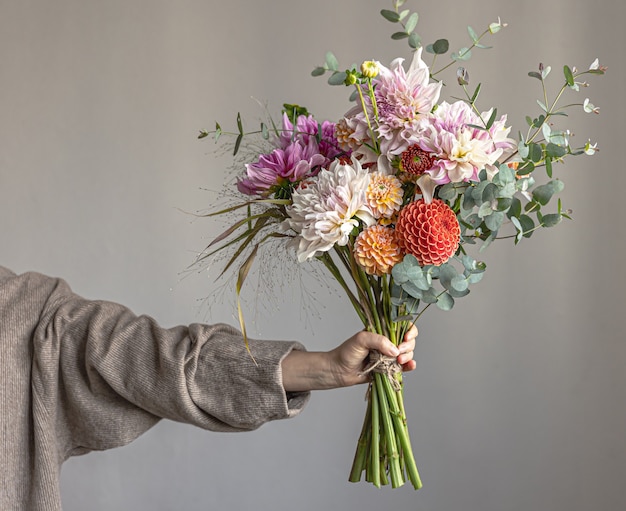 女性は、鮮やかな菊の花、お祝いの花束を持ったお祝いのフラワーアレンジメントを手に持っています。