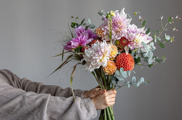 女性は、鮮やかな菊の花、お祝いの花束を持ったお祝いのフラワーアレンジメントを手に持っています。