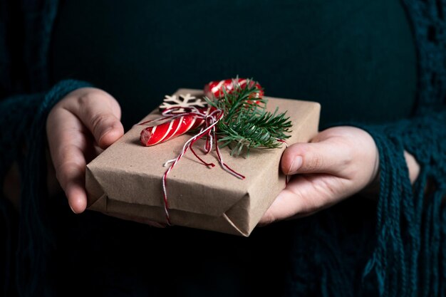 A woman holds in her hands a gift tied with a thread decorated with a sprig of nobilis and a caramel stick