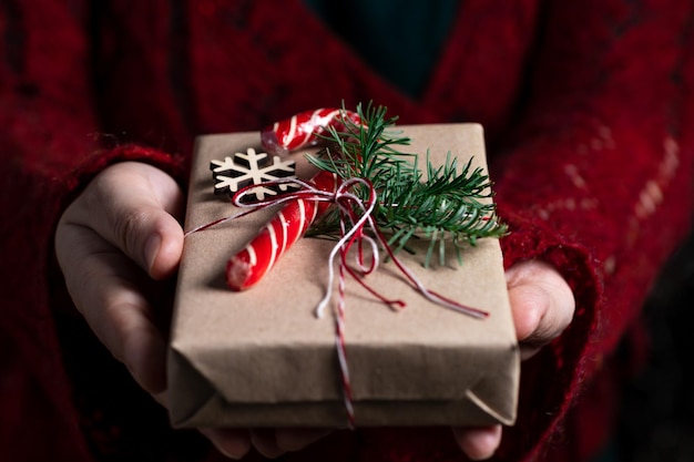 A woman holds in her hands a gift tied with a thread decorated with a sprig of nobilis and a caramel stick