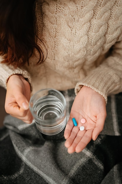 Woman holds in her hands glass of water and pills for colds and flu