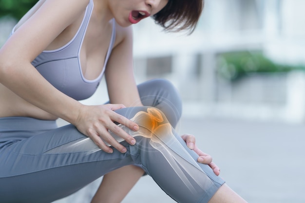 Woman holds her hands to the knee, pain in the knee highlighted in red, medicine, massage concept.