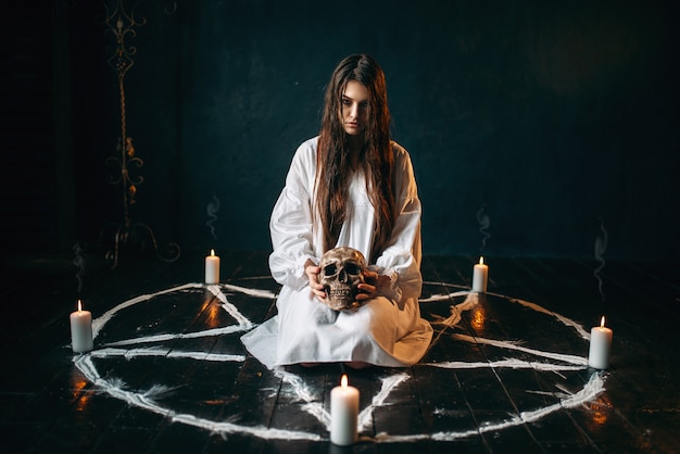 Woman holds human skull in hand, dark magic, witch