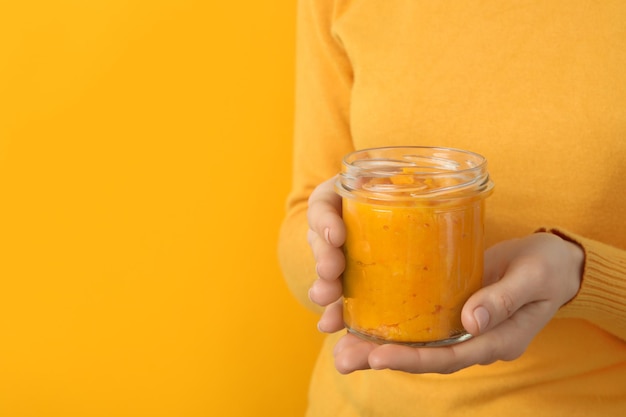 Woman holds jar of pumpkin jam on orange background