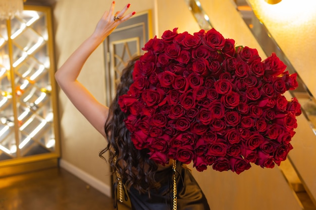 女性は赤いバラの豪華な花束を持っています。