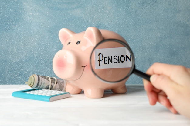 Woman holds magnifier on piggy bank with inscription Pension against blue