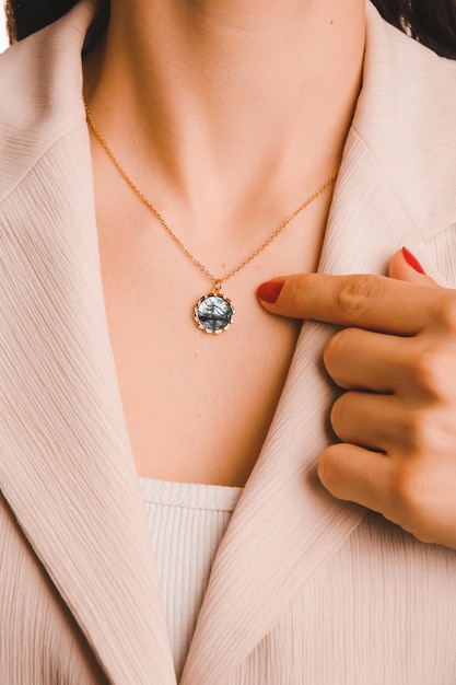 A woman holds a necklace with a blue stone on it.