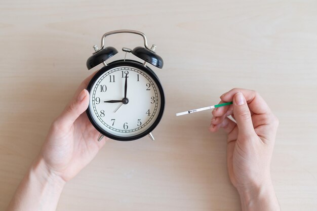 Woman holds negative ovulation test and alarm clock Female fertility biological clock concept Not the right time to conceive a baby