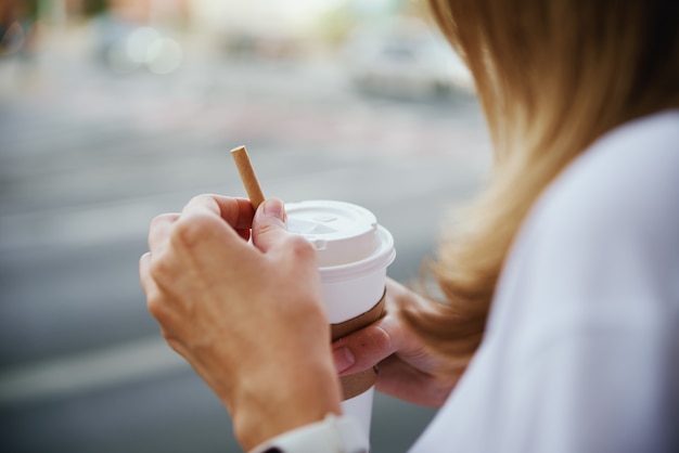 女性は街の通りで紙のコーヒーカップを保持します