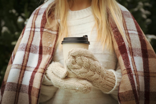 Женщина держит бумажный стаканчик с горячим напитком на открытом воздухе