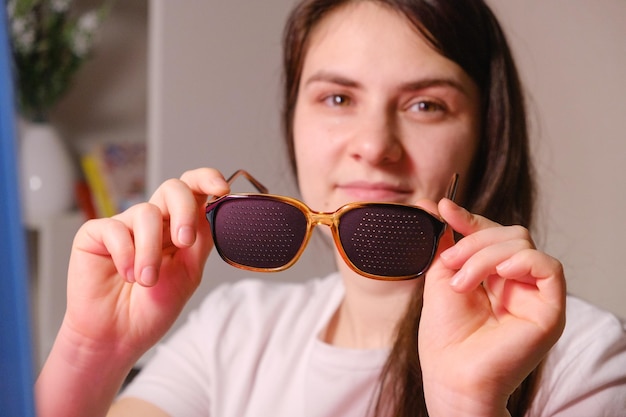 A woman holds perforation glasses to correct visual impairment