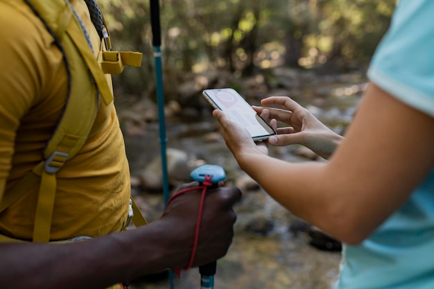 woman holds the phone looking on the map for the correct direction of her path through the mountain she is with her partner looking for the direction