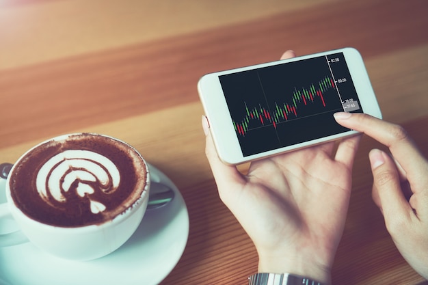 The woman holds the phone on a table with a graphical screen to invest the stock's value. Investment concepts that rely on decision-making information, vintage effect.