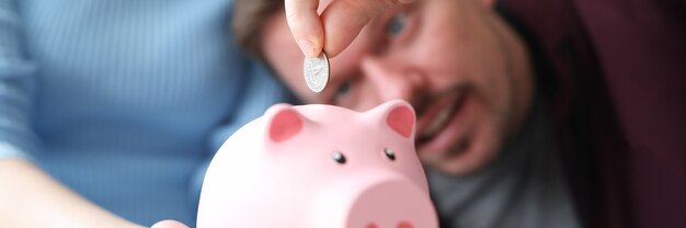 Woman holds pink piggy bank into which man throws coin