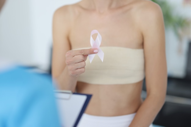 女性は、医師の予約で乳房検査中にピンクリボンを手に持っています