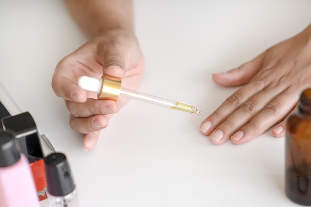 Woman holds pipette with oil to apply to her nails for treatment and strengthening of nails