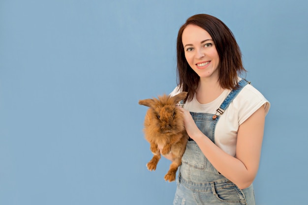 Woman holds rabbit in hands on a blue background.