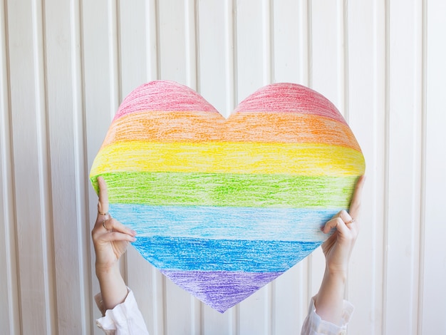 A woman holds a rainbow heart on white wall Symbol of the LGBT community