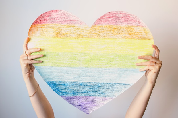 A woman holds a rainbow heart on white wall Symbol of the LGBT community