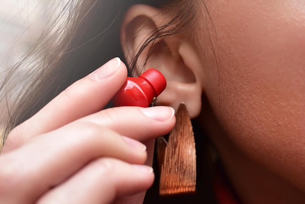 Photo a woman holds a red wireless earphone in her hand bringing it closer to her ear to listen to music close up view